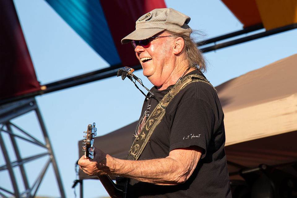 Neil Young smiling, playing guitar on stage