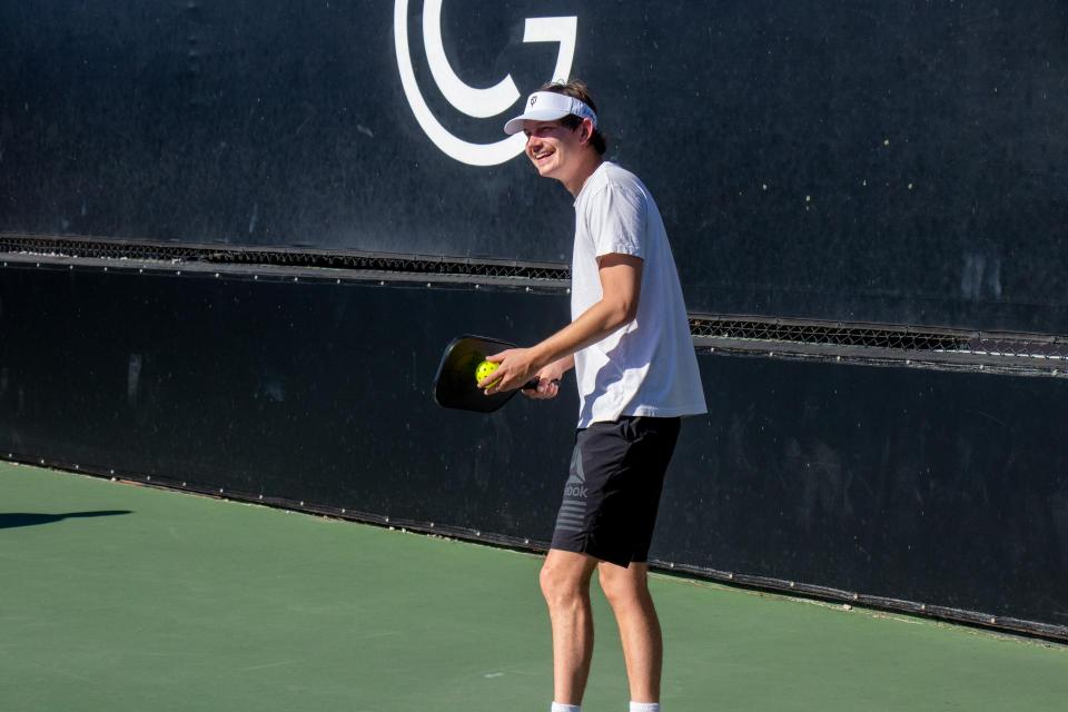 A man with white shirt and navy shorts waits to hit the pickleball back to his aponent. 