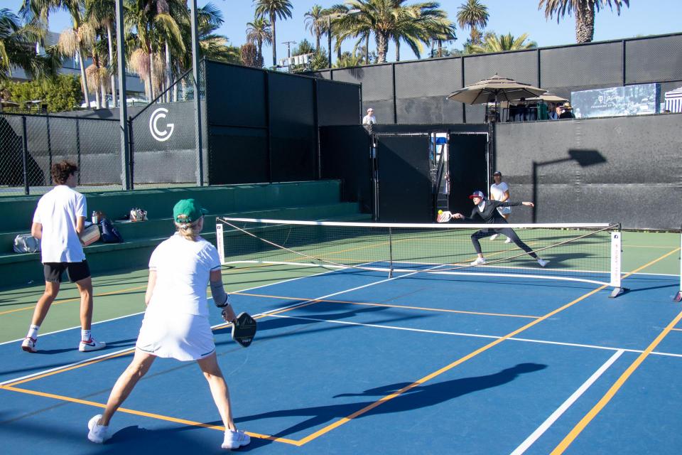 Two men pickleball players photographed from behind return the pickleball to their opponents. 