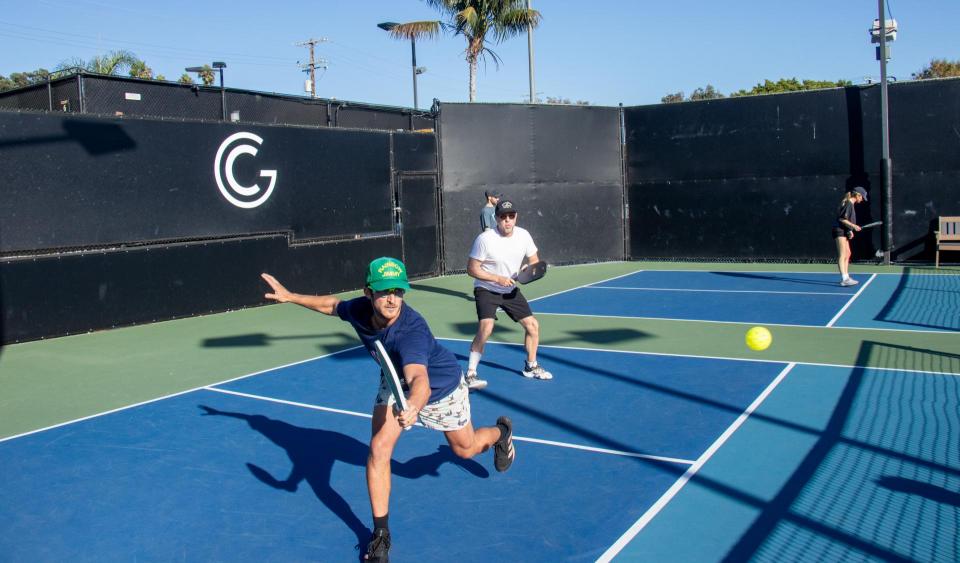 A pickleball player lunges towards the pickleball as he returns the ball across the net. 